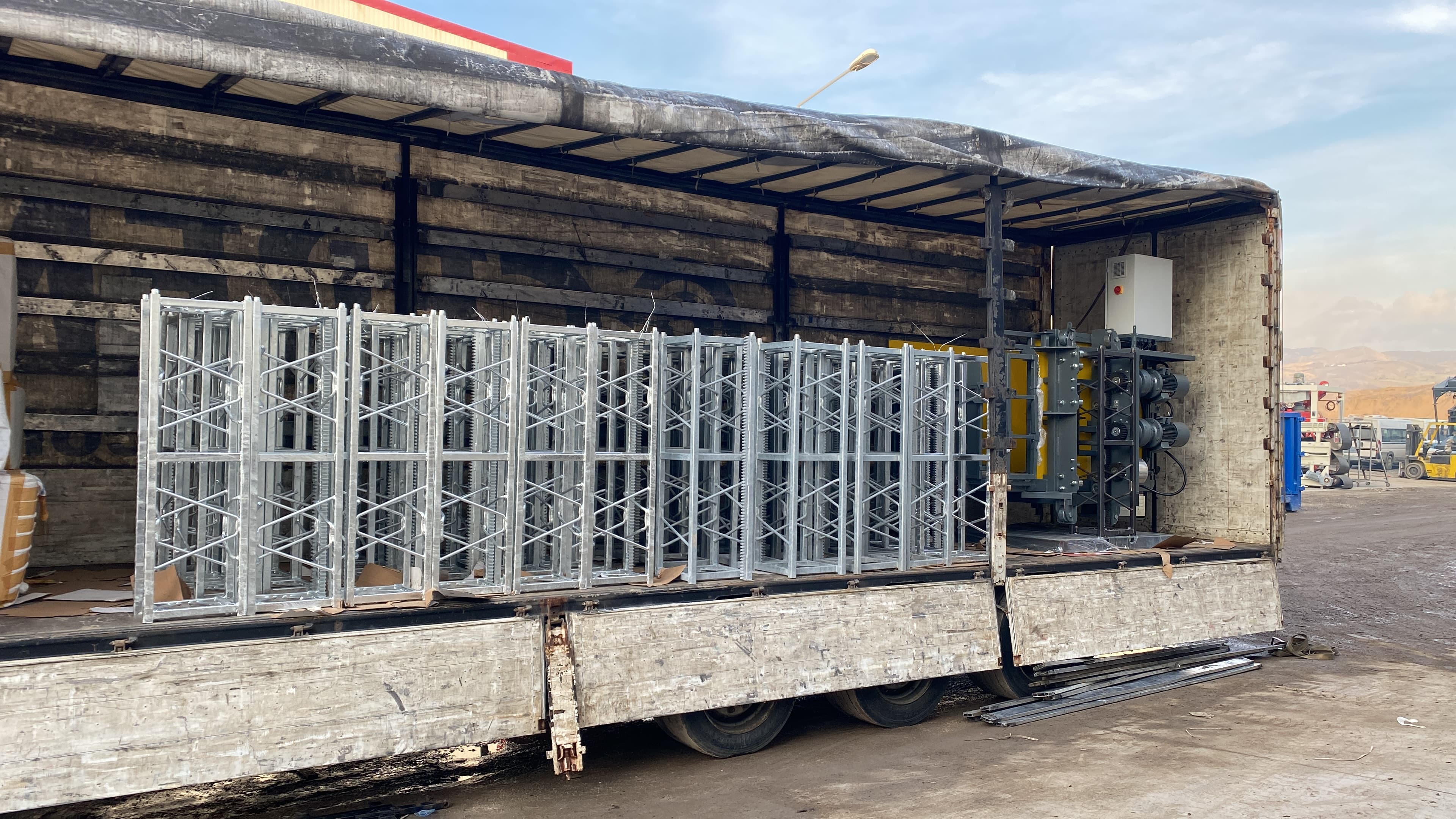 Open trailer loaded with galvanized mast sections and a drive unit prepared for export shipment